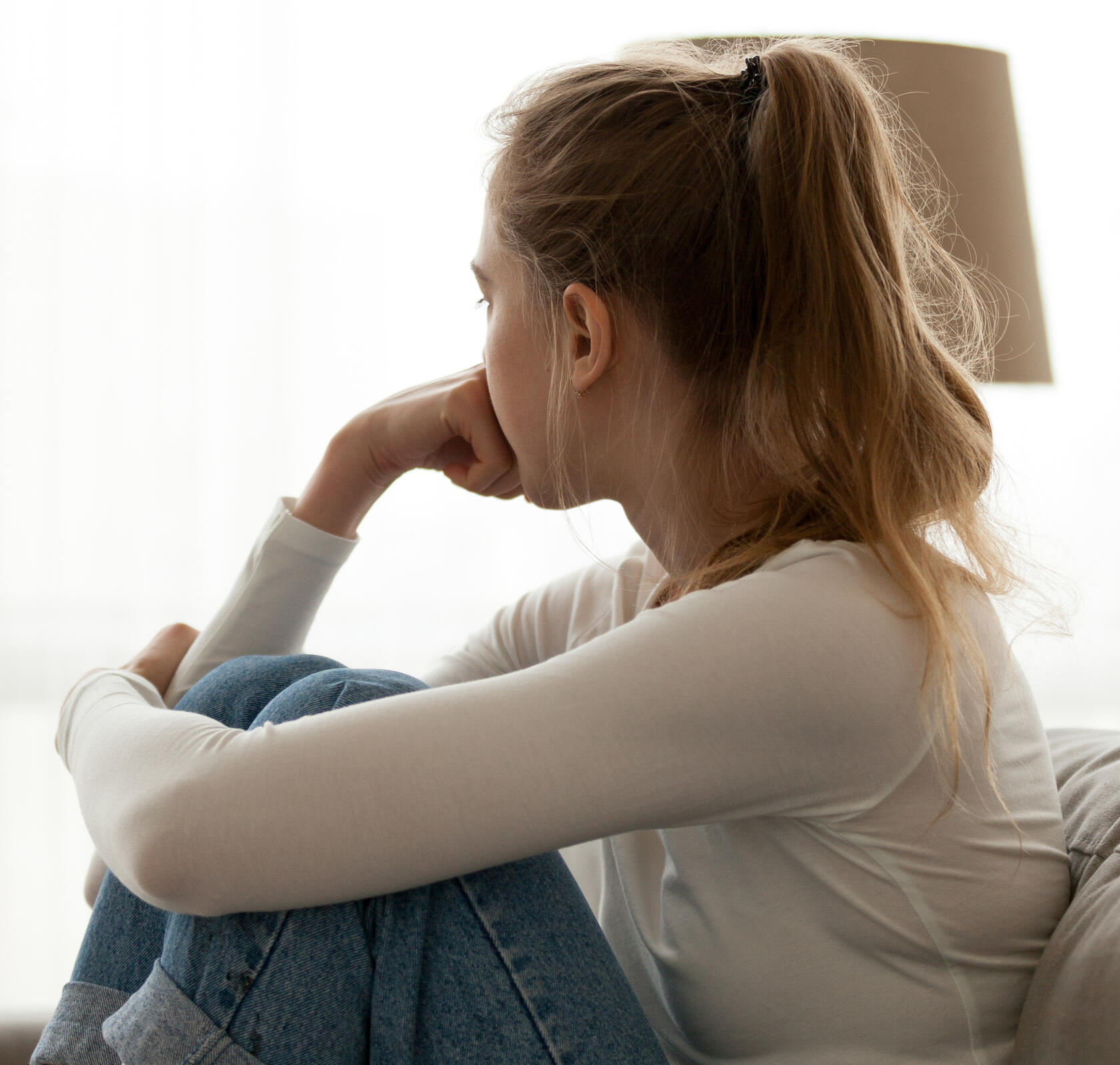 Woman sitting on a sofa looking out a window, appearing deep in thought and worry associated with anxiety