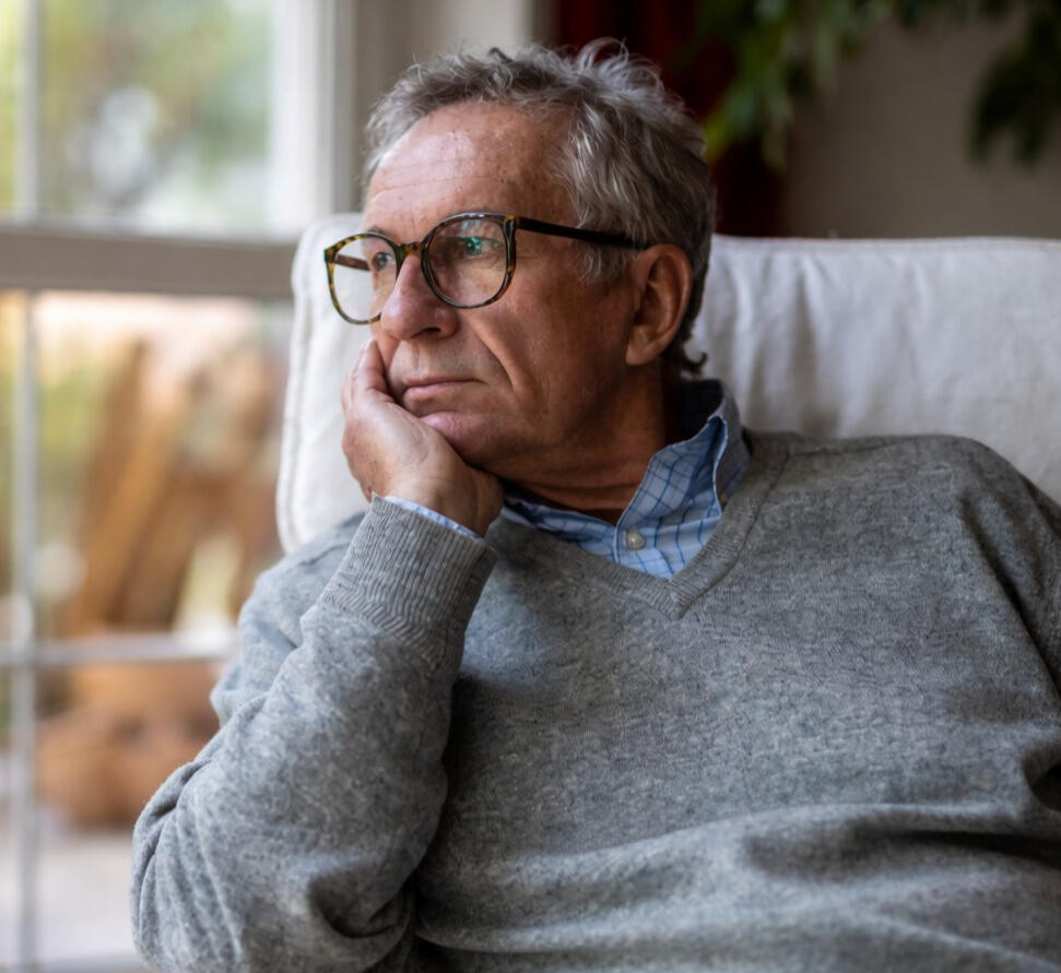 Person sitting on the edge of a bed looking out a window, appearing withdrawn and reflective in a way that suggests depression