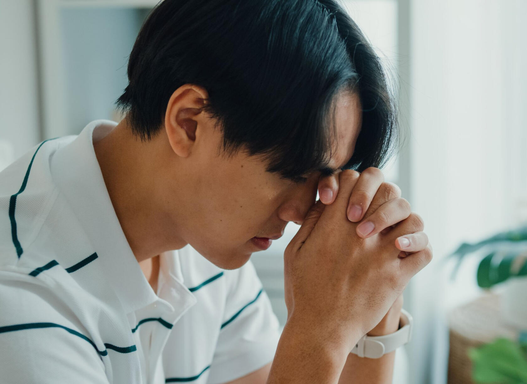 Man sitting with hands folded upwards, appearing overwhelmed and struggling with emotions
